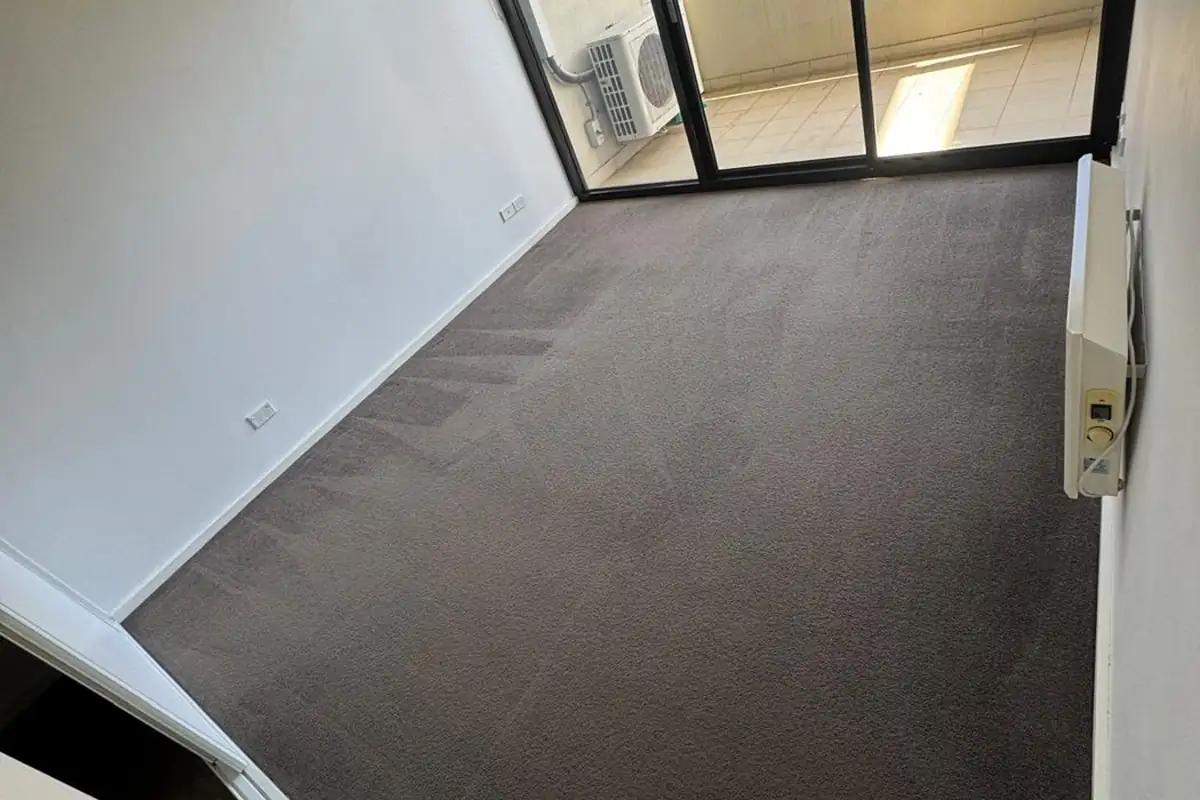 Clean empty bedroom with freshly cleaned carpet and a balcony door after an end of lease clean